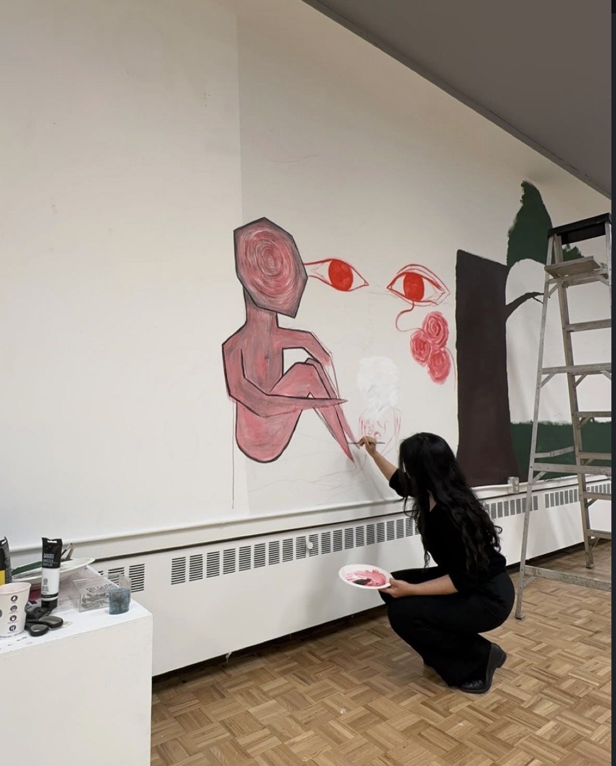 Malika crouched with a palette of pink paint, working on her mural Wall of Roses in a school hallway.